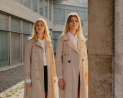 Två kvinnor i ljusa, skräddade trenchcoats framför en modern byggnad